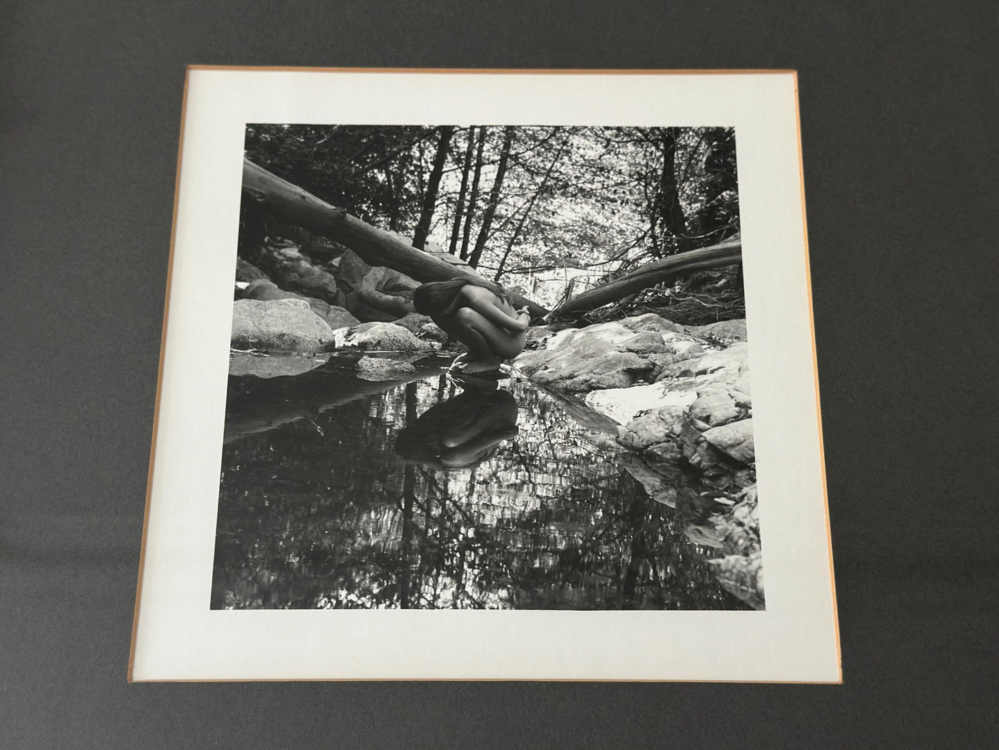 Vintage black and white photograph of a woman crouching in a brook in a vintage frame