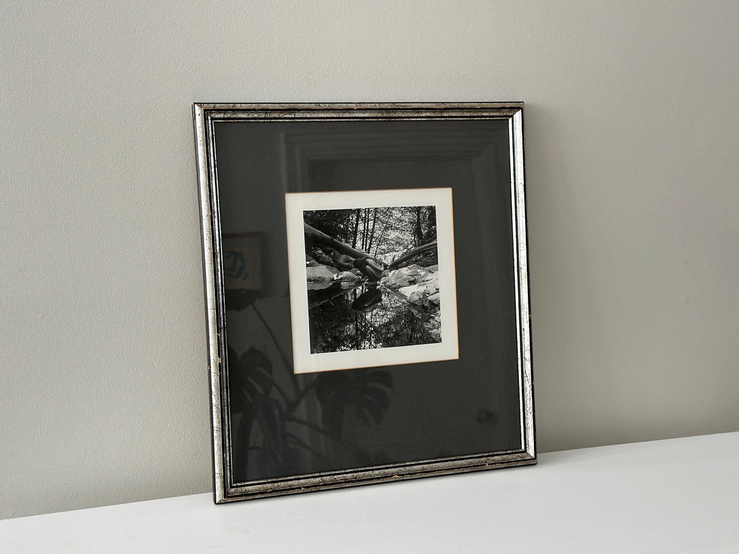 Vintage black and white photograph of a woman crouching in a brook in a vintage frame